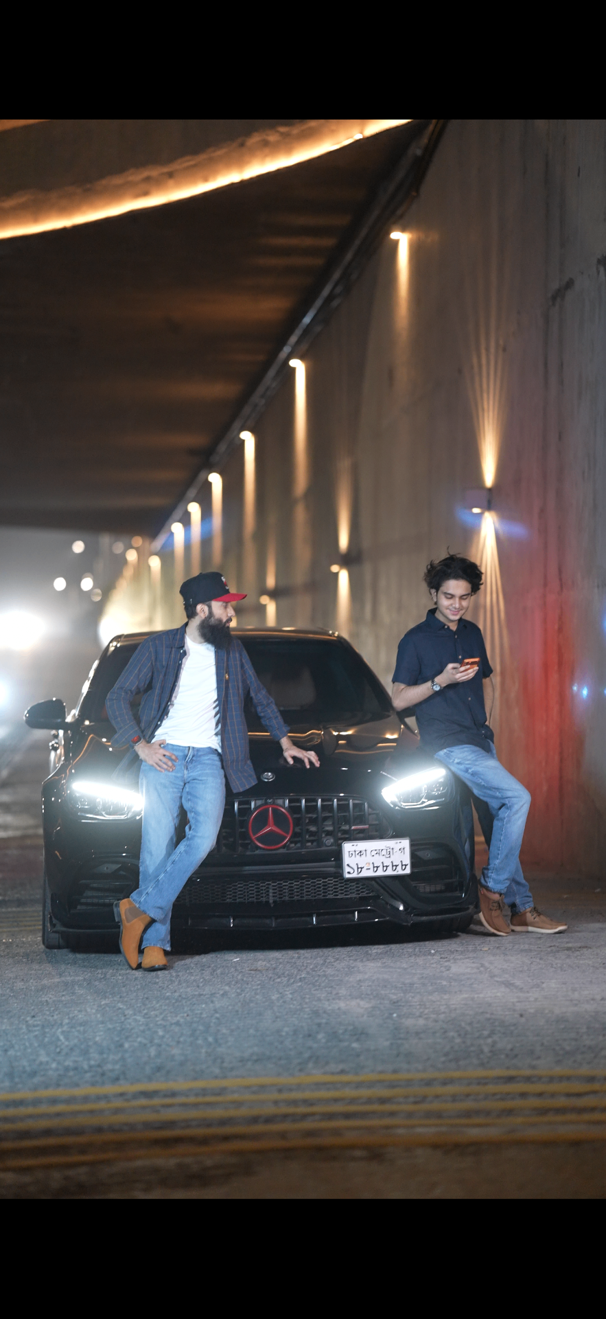 Wahid and his father in front of a black AMG under warm tunnel lights